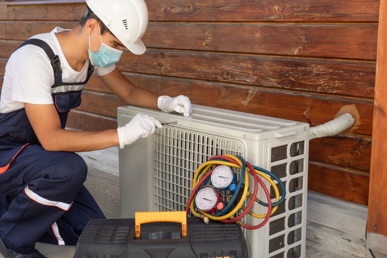 Portrait of a young technician in a disposable protective medical mask and gloves repairing an air conditioner