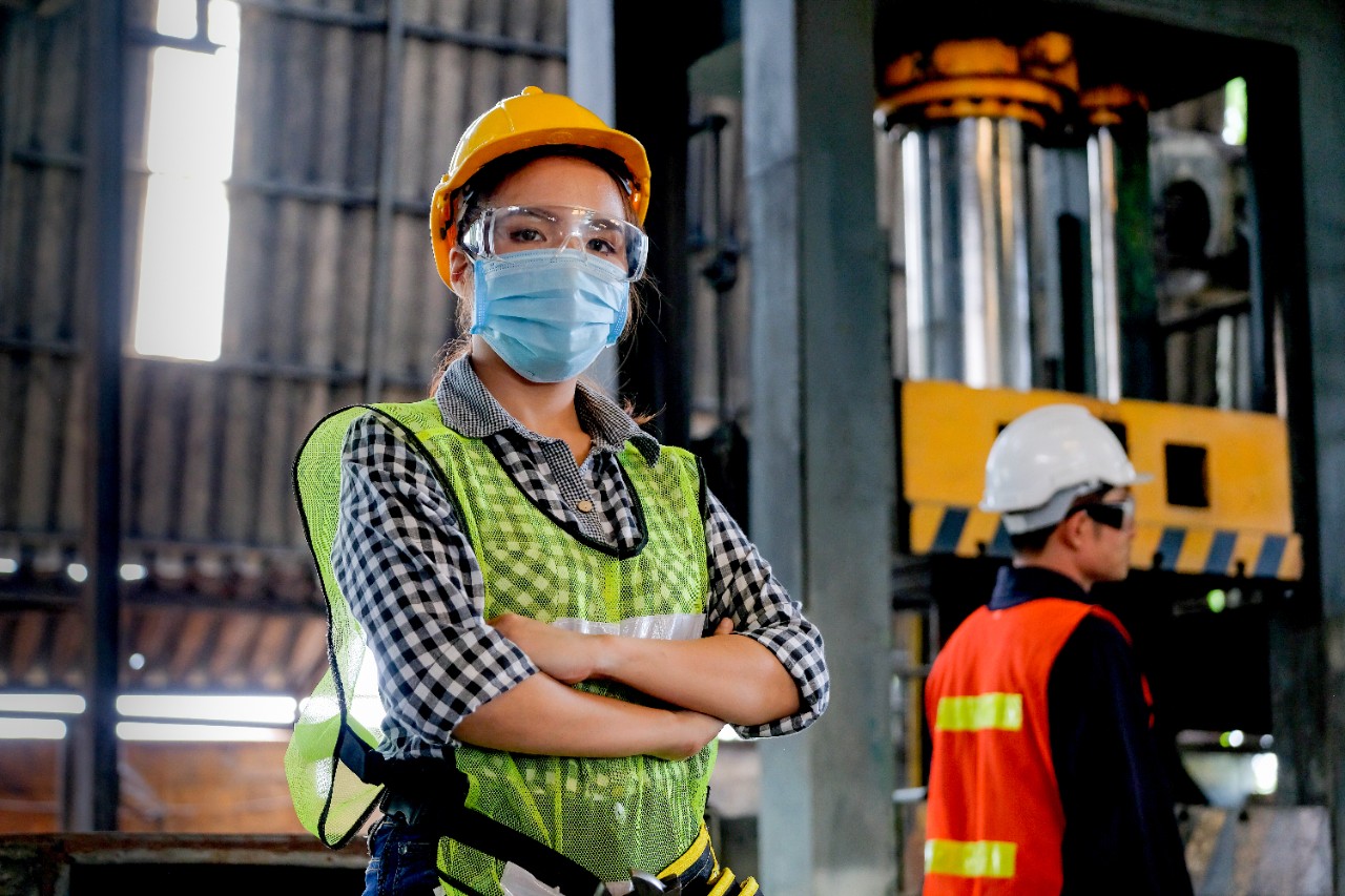 Factory woman worker or technician with hygienic mask stand with confident action with her co-worker  as background.