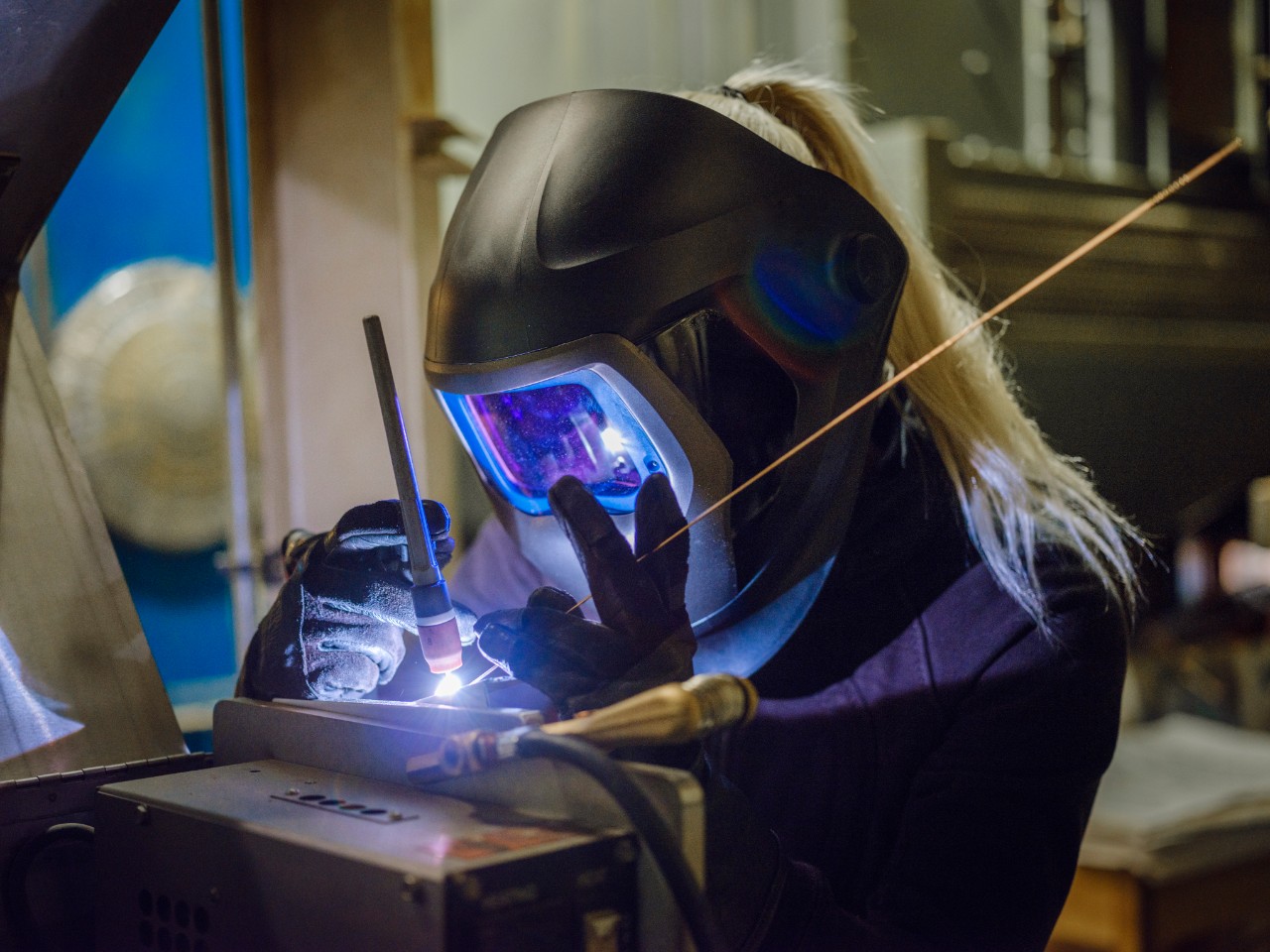 A woman tig welder works in a production facility to repair a piece of equipment.